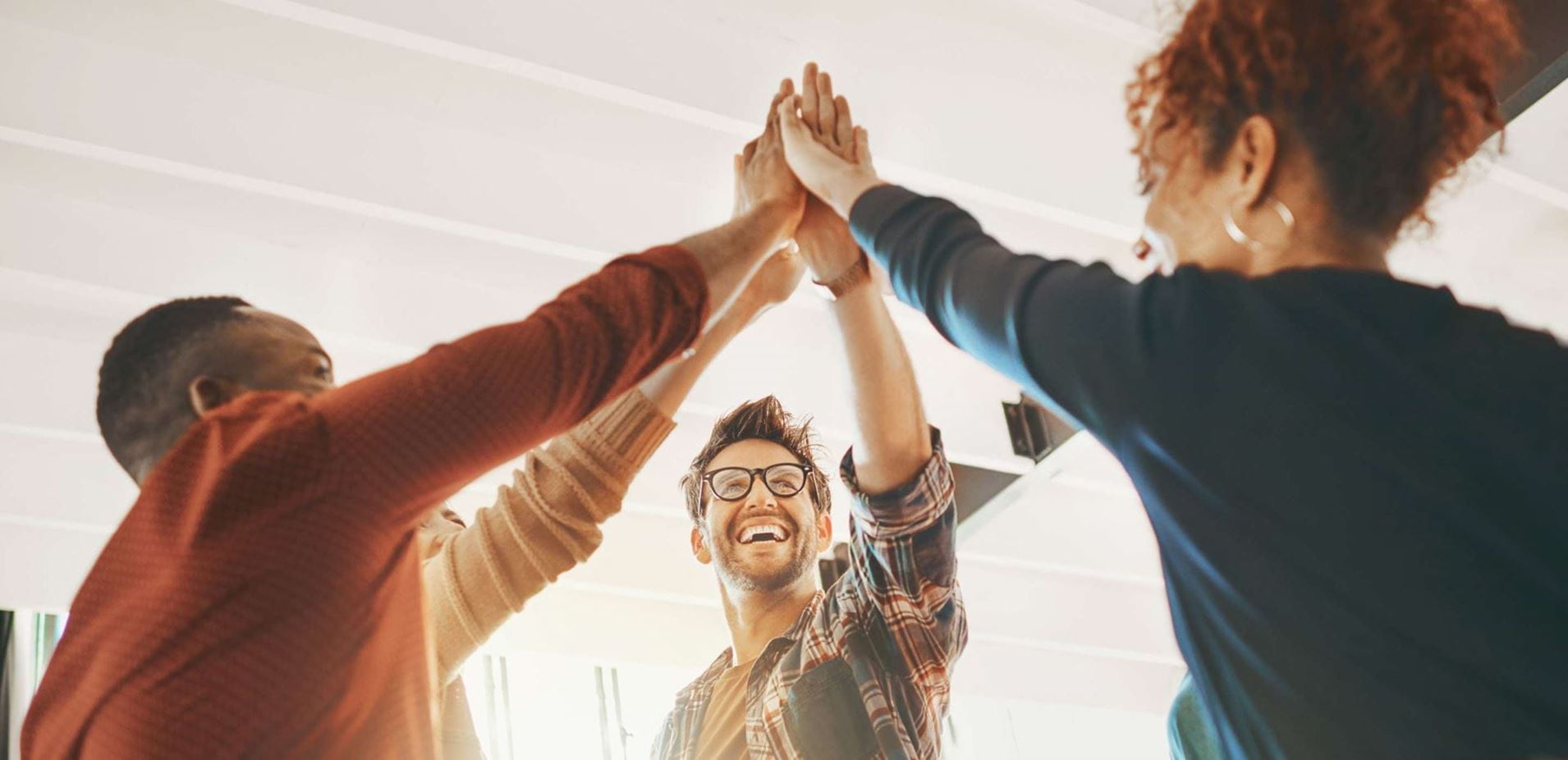 stock image of four young racially diverse office workers giving each other a high five